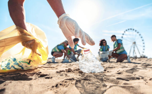 Group of eco volunteers picking up plastic trash on the beach - Activist people collecting garbage protecting the planet - Ocean pollution, environmental conservation and ecology concept