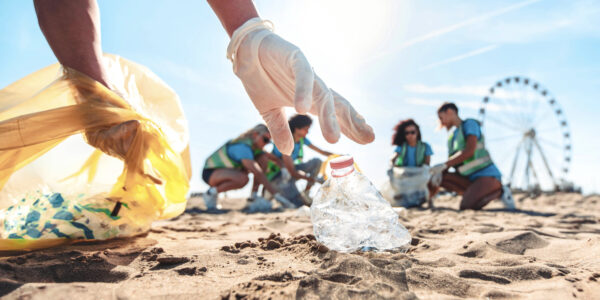Group of eco volunteers picking up plastic trash on the beach - Activist people collecting garbage protecting the planet - Ocean pollution, environmental conservation and ecology concept